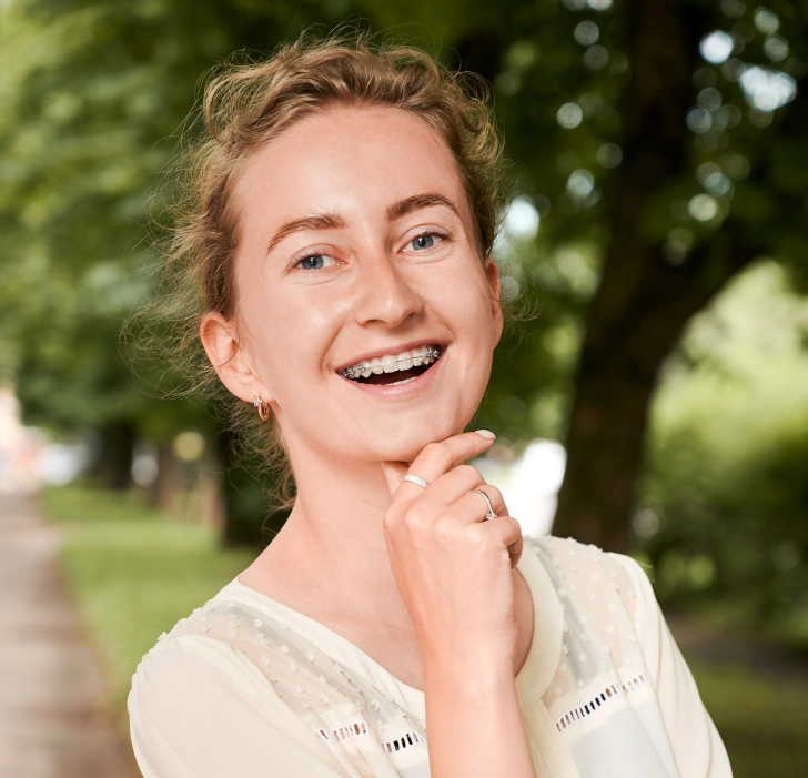 Smiling woman wearing braces outdoors in a park.