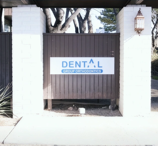 Exterior sign for Dental Group Orthodontics mounted on a wood accent wall between white brick pillars