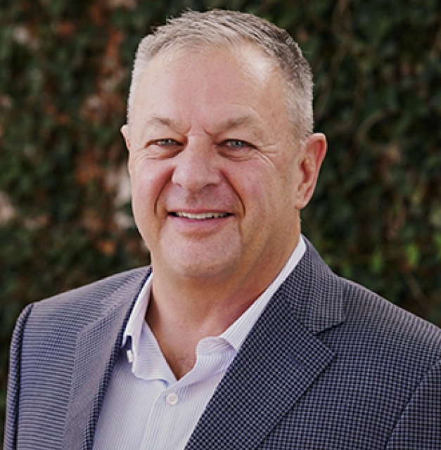 Professional headshot of Dr. Gary Chapman smiling in a gray sport coat against a green foliage background
