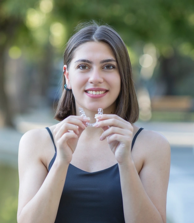 Smiling woman holding a clear aligner tray outdoors