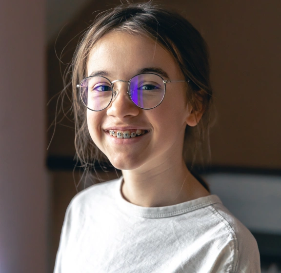 Smiling young girl with glasses and braces wearing a white shirt