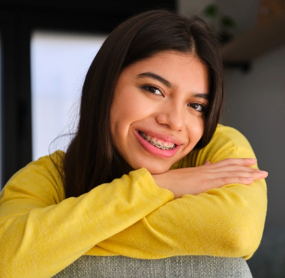 Smiling teen girl with braces resting her chin on her arms wearing a yellow sweater