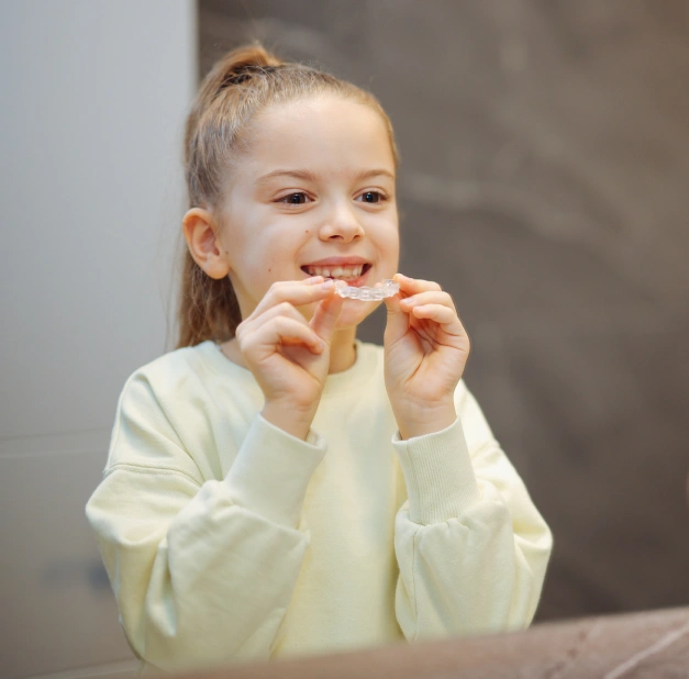 Young girl smiling while holding a clear aligner up to her mouth