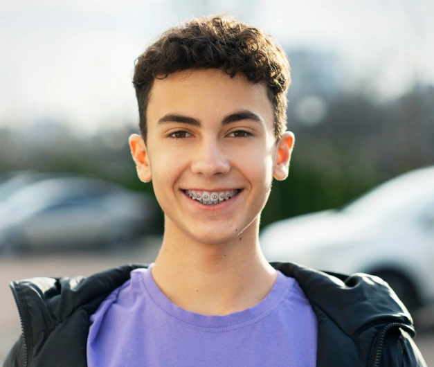 Smiling teenage boy with braces wearing a black jacket over a purple shirt